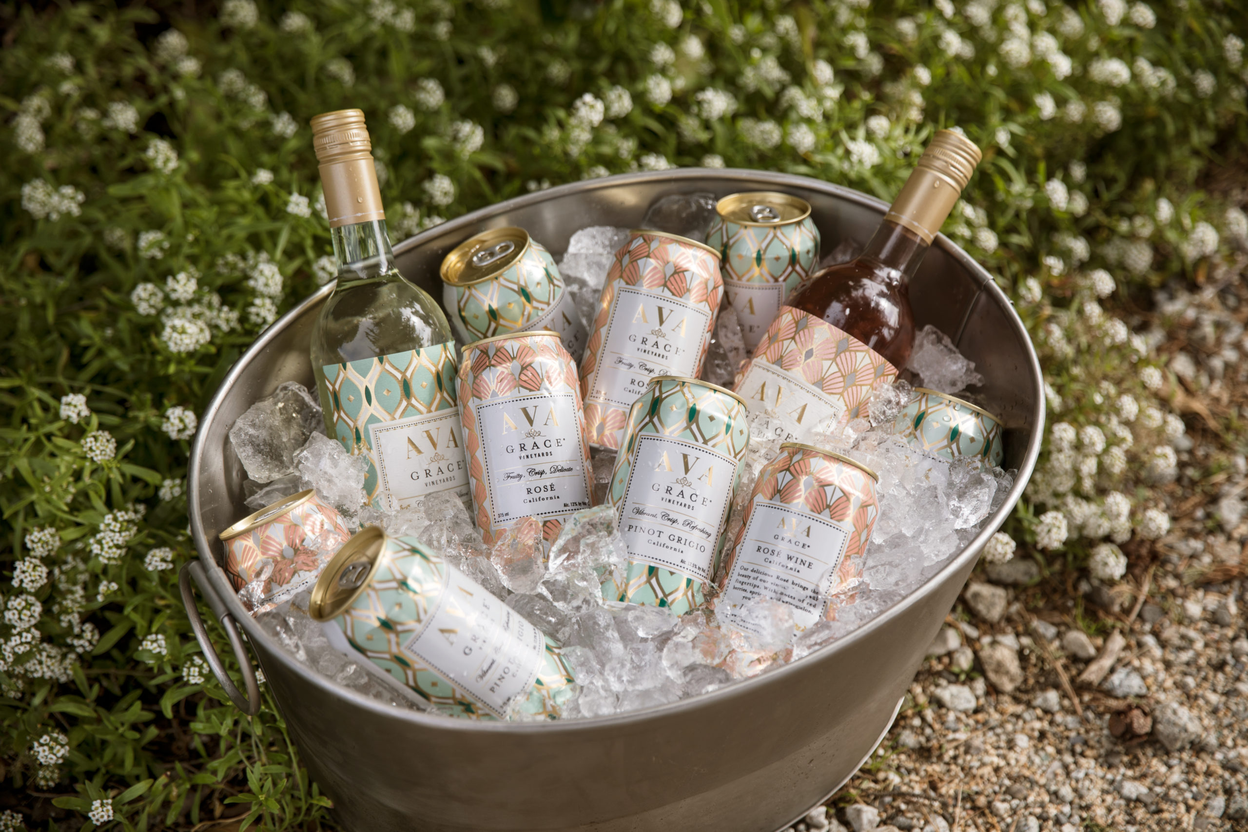 An ice bucket filled with bottles and cans of AVA Grace wines at a summer backyard BBQ.
